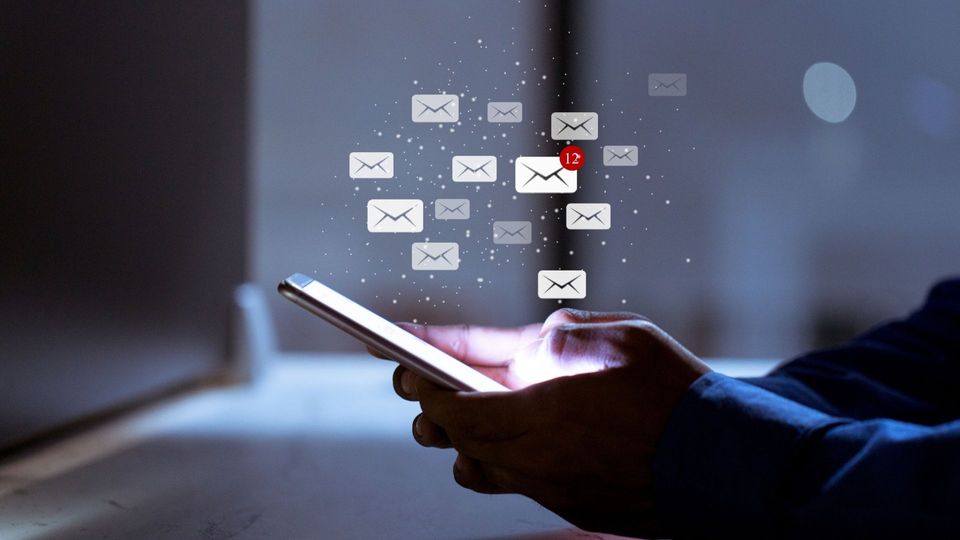 person holding a phone in the dark with the screen on and graphics of email envelopes overlaid