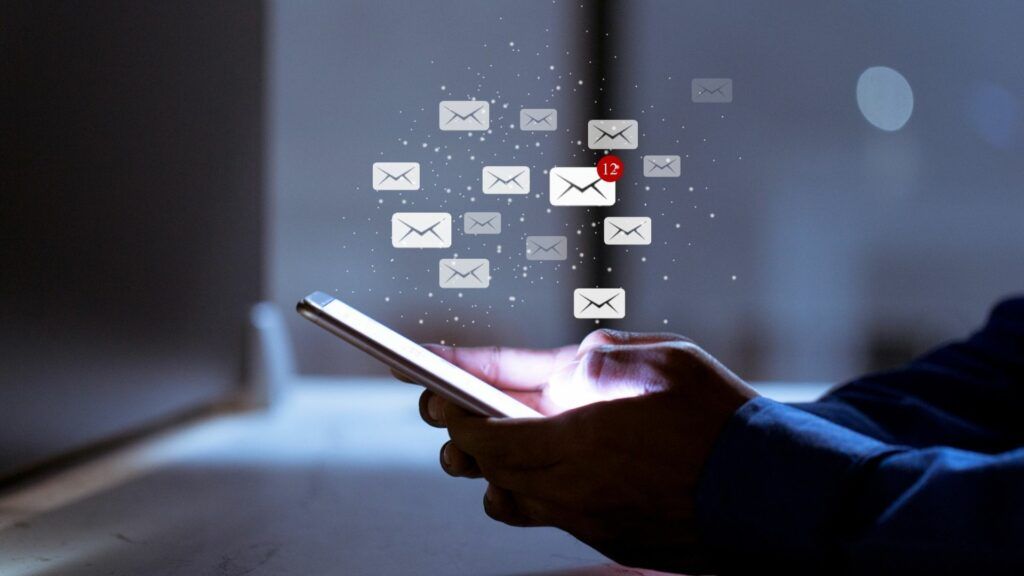 person holding a phone in the dark with the screen on and graphics of email envelopes overlaid